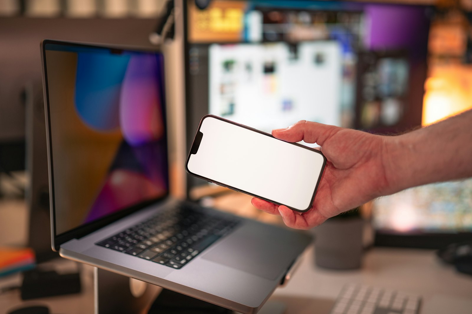 Hand holding a smartphone in front of a laptop